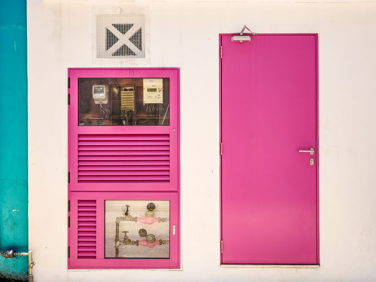 Close-up of a vibrant pink door and utility box on a white wall, showcasing minimalist urban design.