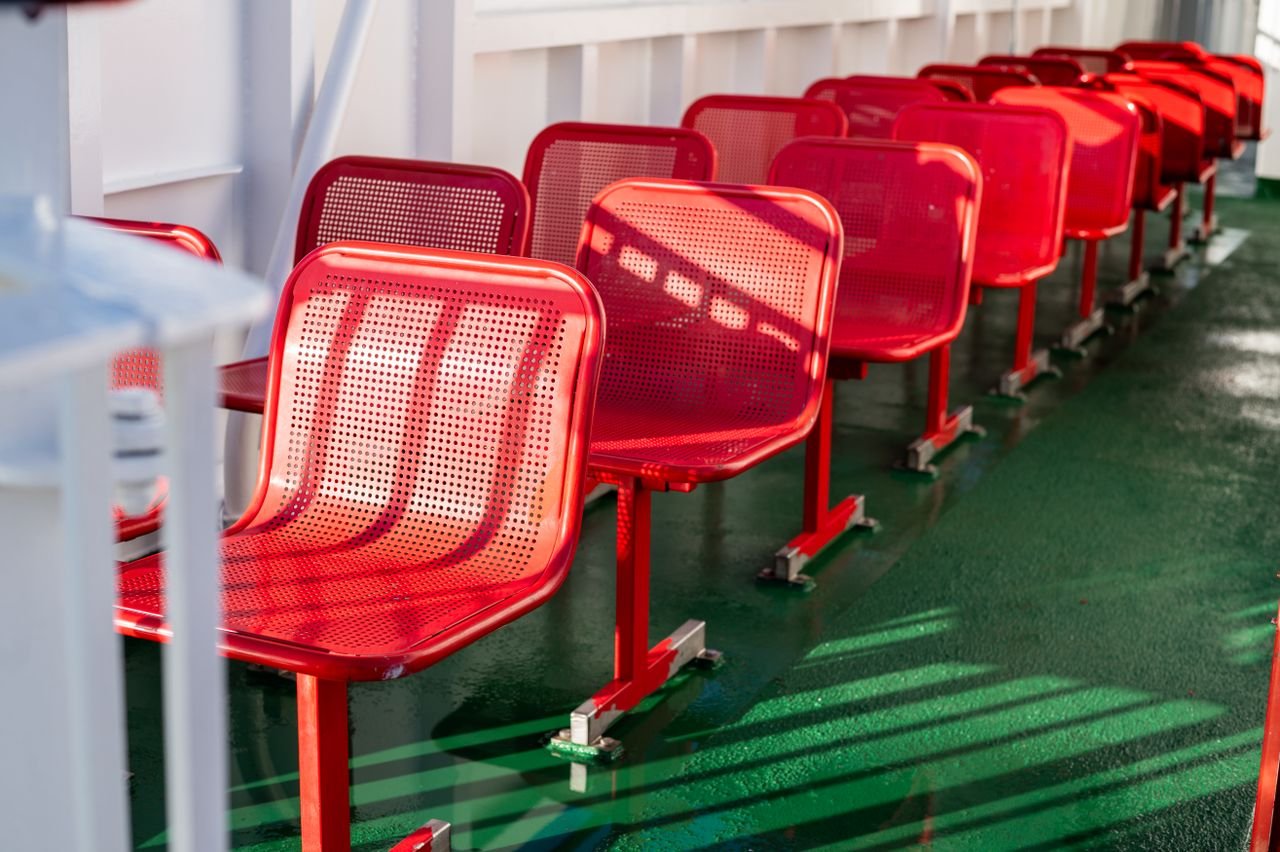 Vibrant red metal chairs lined up on a ferry deck in Scotland, casting unique shadows.