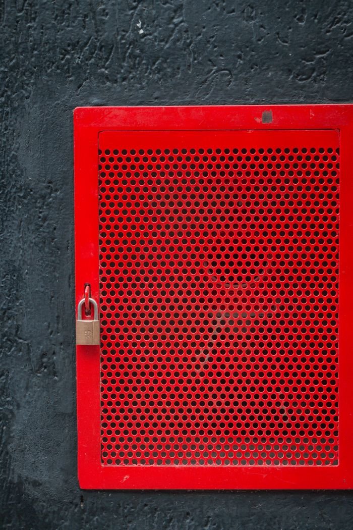 Red perforated metal panel with a padlock on a textured dark background. Industrial design.