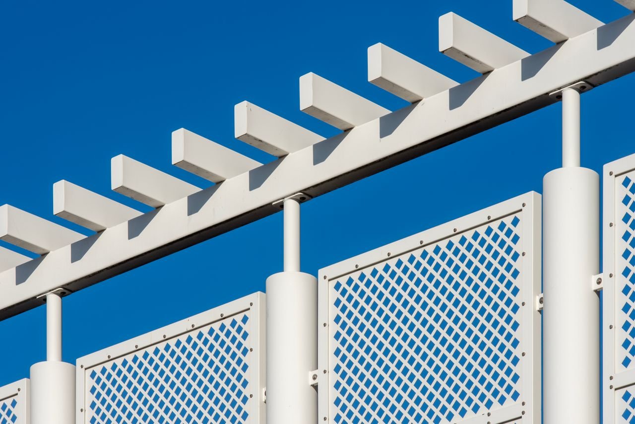 White metal structure with geometric design set against a clear blue sky.