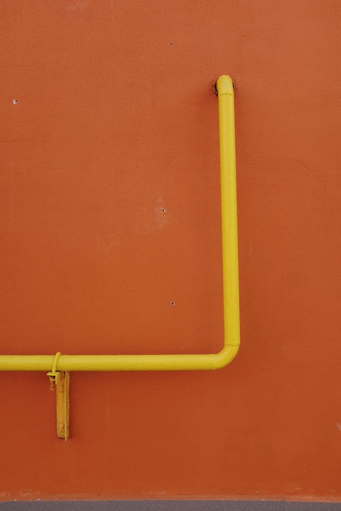 Minimalist shot of a yellow pipe against an orange wall, showcasing color contrast and texture.
