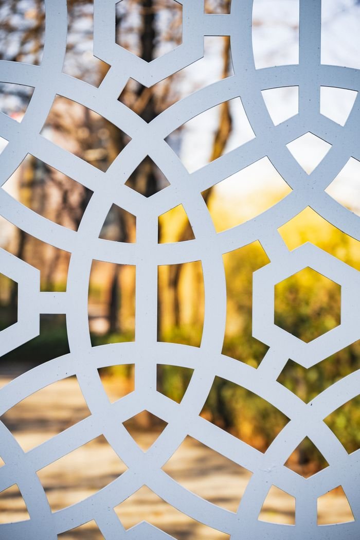 Peaceful autumn park with yellow trees on sunny day through fence with geometric pattern