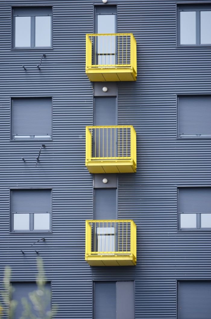 A modern building facade featuring vibrant yellow balconies with closed windows.