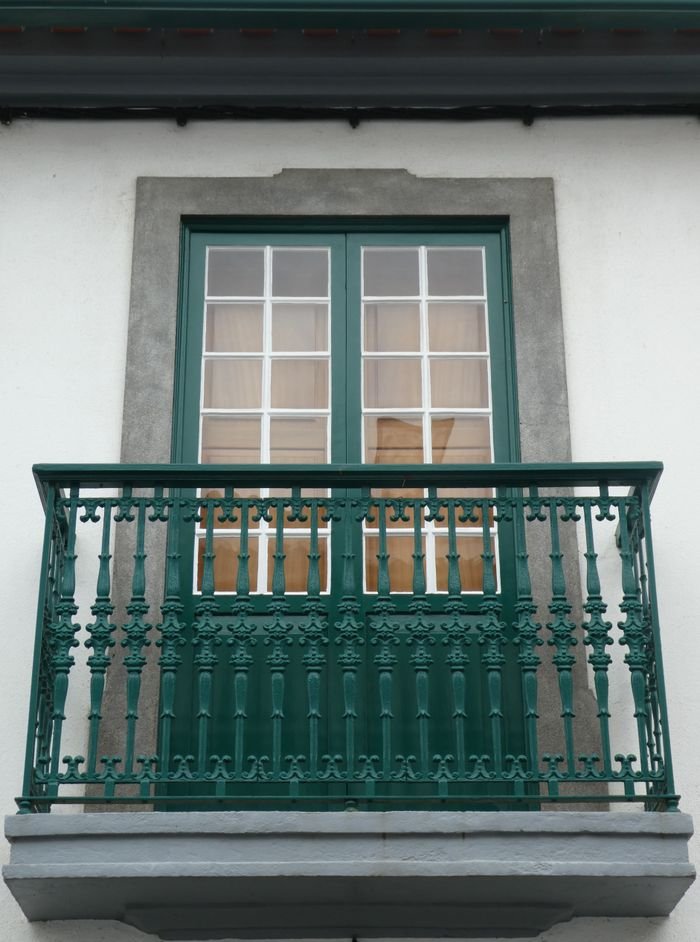Charming balcony with green metal railing and French doors on a white building facade.